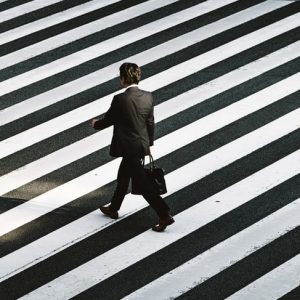 Photo in black and white of man walking on a zebra crossing